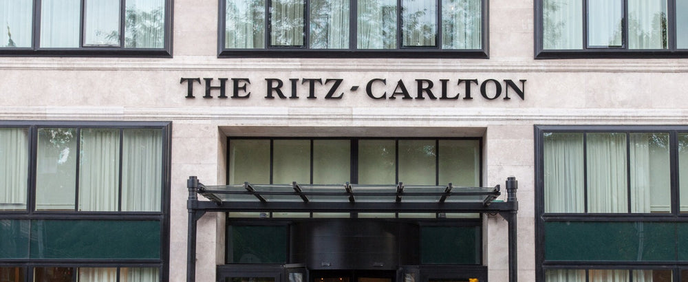 Die edle Fassade des Ritz-Carlton mit eleganten Lettern über dem Hoteleingang, eingefasst in feinen Naturstein. Im Vordergrund der einladende Text 'Welcher Naturstein passt zu Ihnen? Lassen Sie sich inspirieren durch unsere Kunden', der auf die Bedeutung von Qualität und Individualität in der Gestaltung mit Naturstein hinweist